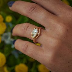 a woman's hand with a ring on it and yellow flowers in the background