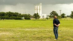 a man standing on top of a lush green field next to a tall white silo