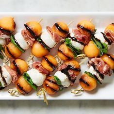 small appetizers with meat, cheese and greens are arranged on a white platter