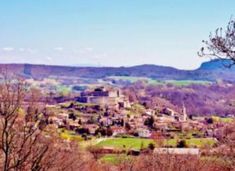 a small village in the middle of some trees and hills with mountains in the background