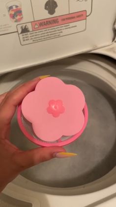 a person is holding a pink object in front of a washing machine with the lid open