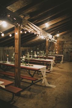 an instagram photo of tables and benches in a barn with lights strung from the ceiling