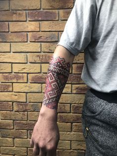 a man with a tattoo on his arm is standing in front of a brick wall