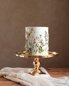 a white and gold cake with flowers on it sitting on top of a wooden table