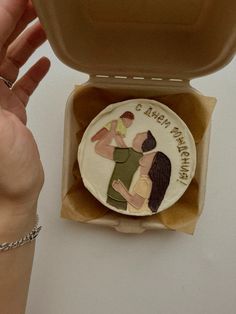 a cake in a box with two people on it and one is holding the lid