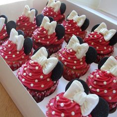 cupcakes with red frosting and white bows are in a box