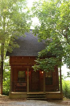 a small cabin in the woods with trees surrounding it and a porch on the front