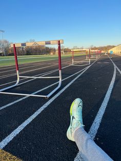 someone's feet resting on the starting line of a running track with hurdles in the background