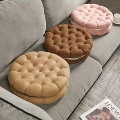 three round cushions sitting on top of a gray couch next to a magazine and coffee cup