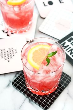 two glasses filled with pink lemonade on top of a table next to coasters