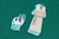 two stickers depicting jesus and a goat on a green carpeted area with grass