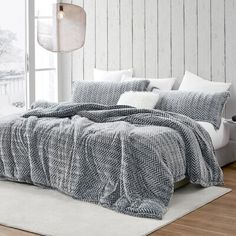 a bedroom with white walls and wood flooring has a large bed covered in a gray blanket