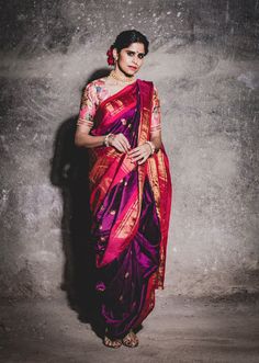 a woman in a pink and purple sari standing against a wall with her hands on her hips