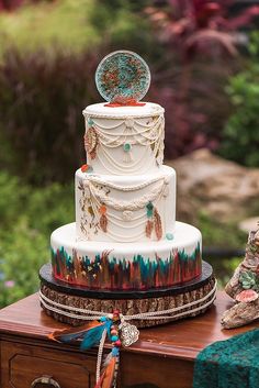 a multi - tiered wedding cake with feathers and beads on the top sits on a wooden table