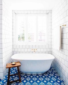 a white bath tub sitting under a window next to a wooden stool in a bathroom