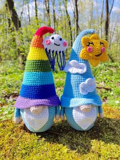 two crocheted gnomes sitting next to each other in the grass with trees behind them