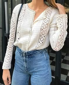 a woman is posing in front of a building wearing jeans and a white shirt with crochet detailing