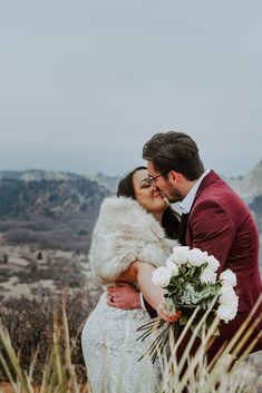 a bride and groom embracing each other in front of the mountains on their wedding day