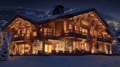 a large wooden house lit up at night with snow on the ground and mountains in the background