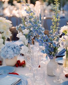 blue and white flowers are in vases on a table with plates, napkins and utensils