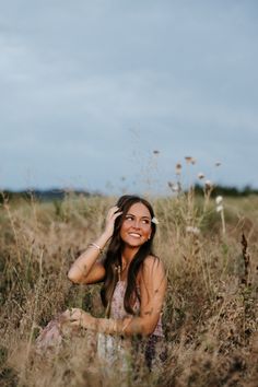 a woman sitting in tall grass with her hand on her head and looking at the camera