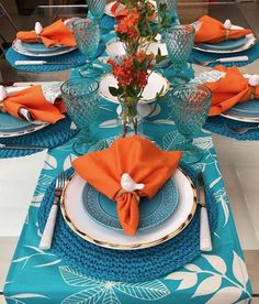 the table is set with blue and white plates, silverware, and orange napkins