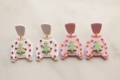 three pairs of earrings with christmas sweaters on them, one is pink and the other is green