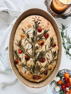 a pie with rosemary sprigs and tomatoes on it in a pan next to other dishes