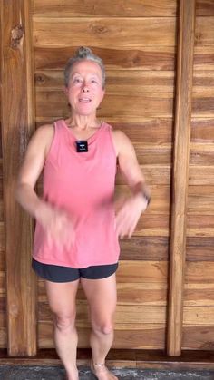 an older woman standing in front of a wooden wall with her hands on her hips