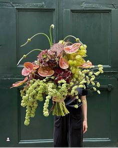 a woman holding a large bouquet of flowers in front of a green door with her hands behind her back