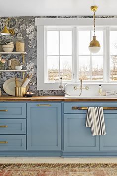 a kitchen with blue cabinets and gold pulls on the handles, white sink and window