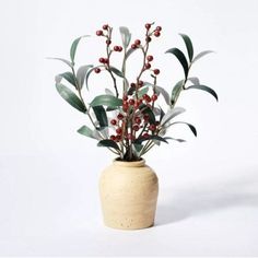 a white vase filled with red berries and greenery on top of a white table