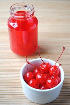 a small white bowl filled with cherries next to a jar of jam on a wooden table