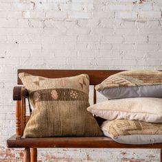 a wooden bench with pillows on it and a brick wall in the backround