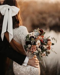 a bride and groom embracing each other in front of a lake with flowers on it