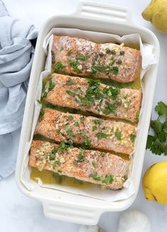 cooked salmon in a white casserole dish with lemons and parsley