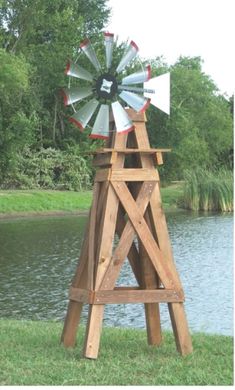 a wooden windmill sitting on top of a lush green field next to a body of water