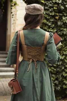 a woman is walking down the street with her back to the camera, wearing a green dress and brown hat