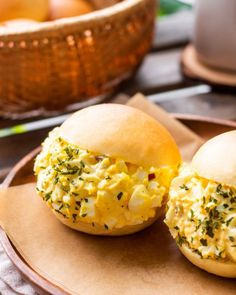 two rolls filled with scrambled eggs on top of a brown plate next to an orange bowl