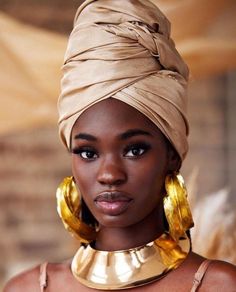 a woman wearing gold jewelry and a turban on her head is looking at the camera