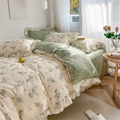 a bed with green and white comforters in a room next to a table with flowers on it