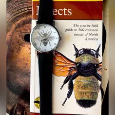 a book with a watch on top of it next to a bee and a statue