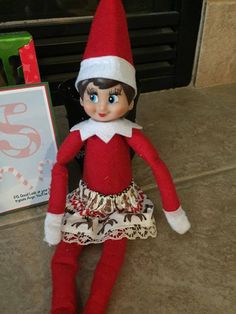 an elf doll sitting on the floor next to a christmas card and a small box