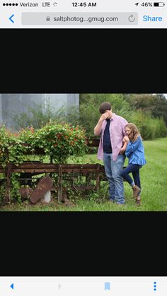 a man and woman standing next to each other in front of a wooden bench with flowers on it