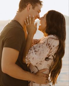 a man and woman kissing each other in front of the ocean