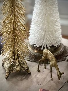 two gold and white christmas trees are on a table next to each other, one with a deer figure