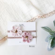 two pink crocheted flowers are on top of a card next to a plant