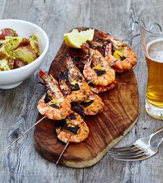 there is a wooden cutting board with shrimp on it and a glass of beer next to it