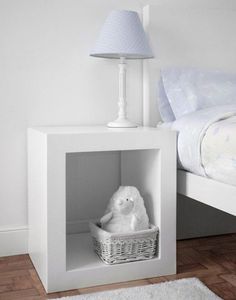 a white teddy bear sitting in a basket under a lamp next to a small bed