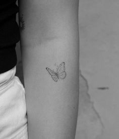 a black and white photo of a butterfly tattoo on the left inner arm, with an outline of a butterfly